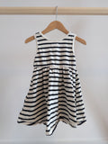 Pale yellow sleeveless baby romper with button closure on the legs, hanging on a wooden hanger.